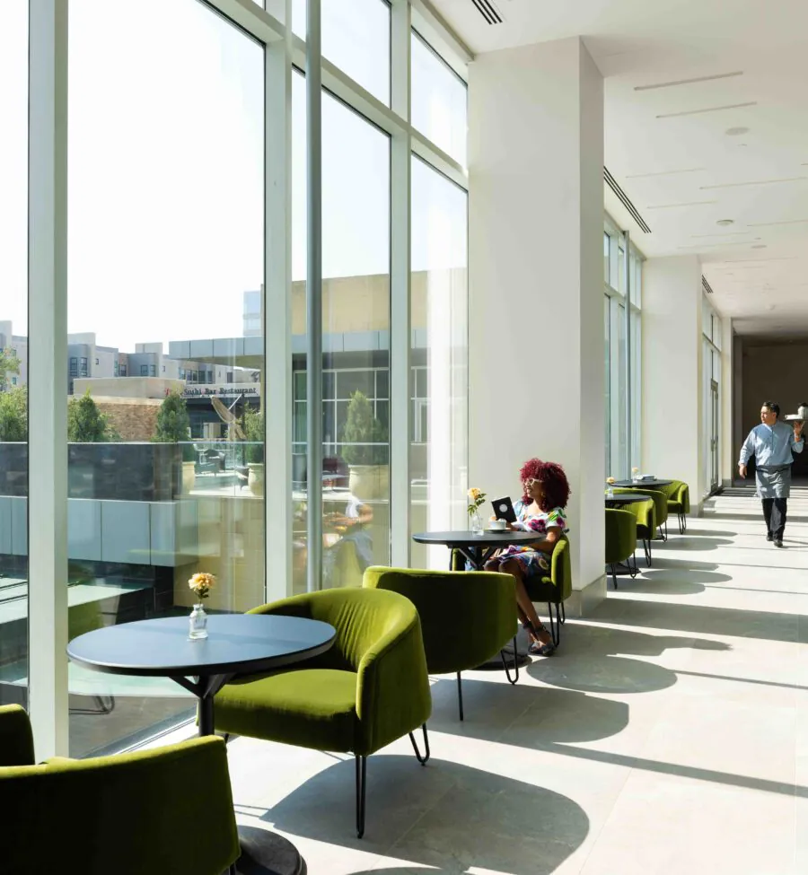 Glas walled hallwaz with green chairs and small round tables.